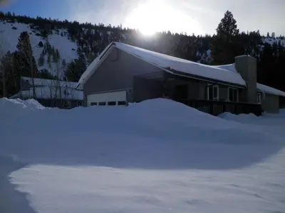 a house covered in snow with the sun behind it at Elk House in June Lake