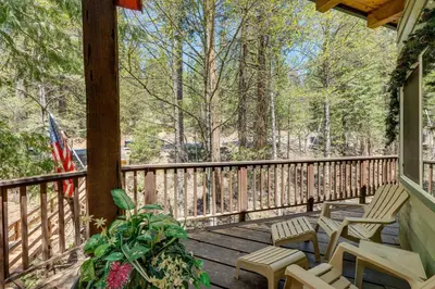 a porch with chairs and a flag and trees at Creekside Cabin By Calaveras Big Trees State Park in Camp Connell
