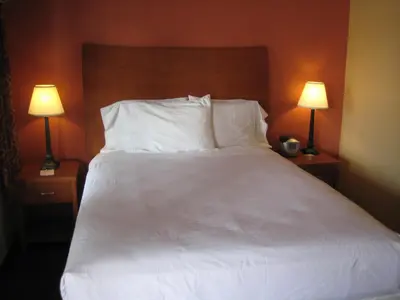 a bed with white sheets and pillows and two lamps at Americas Best Value Inn - Porterville in Porterville