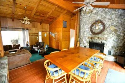 a living room with a wooden table and a stone fireplace at Johnson Lake FrontReduced Nightly Rates in Bass Lake