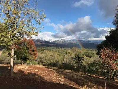 a rainbow in the sky over a field with trees at Morning Star Vista near Yosemite - countryside with mountain views in Mariposa