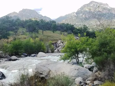 a river with rocks and trees and mountains in the background at **Kaweah River House** - 1/2 Mile to Sequoia Park in Three Rivers