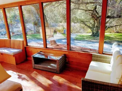 a living room with large windows and a white couch at Sequoia River House, close to SNP, 2 Decks on Amazing River on 7acres in Three Rivers
