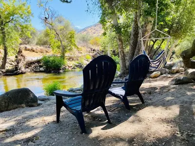 two chairs sitting next to a river with a swing at Sequoia Cabin by the River in Three Rivers