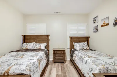 two beds in a room with white walls and two windows at Sunny Turlock Cottage Walk to Downtown! in Turlock