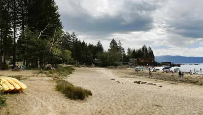 a sandy beach with a group of people and a body of water at Agate Bay Gem by Tahoe Getaways - Charming Getaway with Cozy Fireplace Near Hiking and Biking Trails in Tahoe Vista