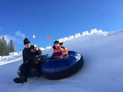 two people riding on a tube in the snow at Camp Telemark by Tahoe Getaways - Pet-Friendly 3 BR in Tahoe Donner with Hot Tub & Wood Fireplace in Truckee