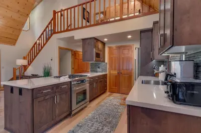 a large kitchen with wooden cabinets and a staircase at Cottonwood by Tahoe Getaways - 3BR Tahoe Donner with 2 Bonus Rooms, Hot Tub, Fireplace, Ping Pong & HOA Amenities in Truckee