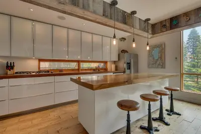 a kitchen with white cabinets and a counter with stools at Mod Haus by Tahoe Getaways - Mountain Modern West Shore Home w Private Beach and Pier, Near Skiing in Homewood