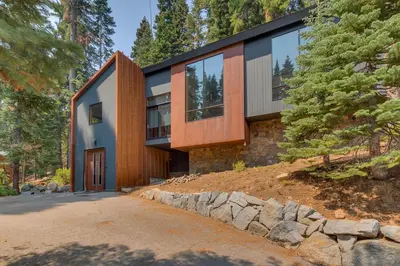 a house in the woods with a stone wall at Mod Haus by Tahoe Getaways - Mountain Modern West Shore Home w Private Beach and Pier, Near Skiing in Homewood