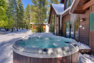 a hot tub in the snow in front of a house at Tippy Canoe by Tahoe Getaways - 4BR West Shore w Private Hot Tub,, Sauna, EV & Walking Distance to Trailhead in Tahoma
