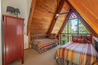 a attic bedroom with two beds and a large window at Ember Ridge Retreat by Tahoe Getaways - 3BR Pet-Friendly Carnelian Bay Rental w Fenced Yard, Ping Pong, Hot Tub, Near Northstar in Carnelian Bay