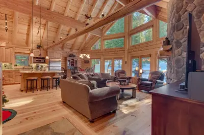 a living room and kitchen with a stone wall at Lodgepole Retreat - A Gorgeous Classic 3BR Log Cabin with Private Hot Tub in Truckee