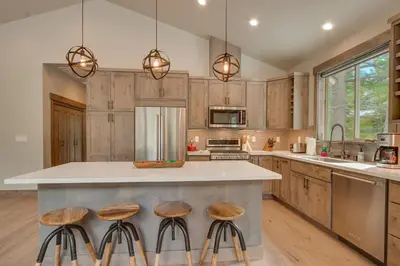 a kitchen with wooden cabinets and a island with stools at Sunrise Abode at Tahoe Donner - Luxurious New Build, Soaking Tub, HOA Amenities in Truckee