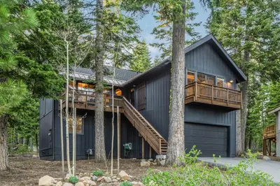 a black house in the woods with a deck at Timber Grove at Tahoe Park - Gorgeous 4BR Cabin - Tahoe Park HOA, Pets OK, Near Skiing in Tahoe City