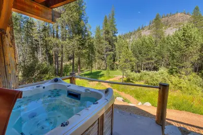 a hot tub on a porch with a view of a forest at Bullshead Lodge- Luxury Estate, 4 Acres on River, Hot Tub, Minutes from the Slopes! in Olympic Valley