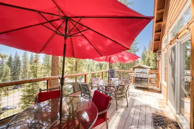 a deck with tables and chairs and a red umbrella at Fawn View by Tahoe Getaways - Spacious 5 BR w Pool Table-Short Drive to Northstar in Tahoe Vista