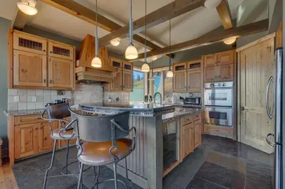 a kitchen with wooden cabinets and a island with bar stools at Grand Vista Lodge by Tahoe Getaways - 5 BR with Stunning Views, Pool Table, Private Hot Tub & HOA Pool! in Truckee