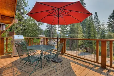 a table and chairs on a deck with a red umbrella at Summit Solitude at Palisade Tahoe - Charming 5BR w Foosball & Shuffleboard Table & Pet Friendly in Olympic Valley