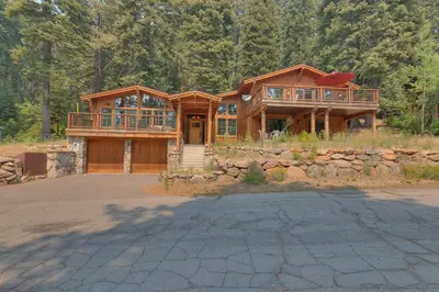 a large wooden house with a stone wall at Summit Solitude at Palisade Tahoe - Charming 5BR w Foosball & Shuffleboard Table & Pet Friendly in Olympic Valley