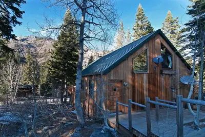 a small wooden cabin in the woods with trees at Alpine Darling- Hot Tub- Pet Friendly- 3 Minute Drive to Palisades Tahoe in Alpine Meadows