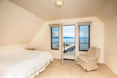 a bedroom with a bed and a chair and windows at Lakeside Escape - Beautiful Lakefront, Pier, Wood Fireplace, Private Hot Tub in Tahoe Vista