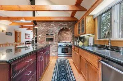 a kitchen with wooden cabinets and a brick wall at Lupine Lodge at Tahoe Park on the West Shore - Hot Tub, Beach Access, Near Ski Resorts! in Tahoe City