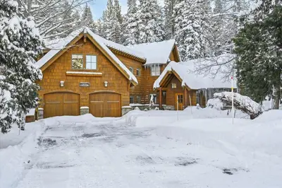 a wooden house with a garage in the snow at Silverado Lodge at Palisades - 4BR w Private Hot Tub & Ski Shuttle in Olympic Valley