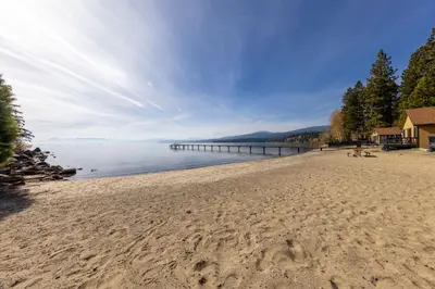 a sandy beach with a pier in the water at Sandy Cove on the North Shore -Lakeside Cottage with Pier Beach, and HOA Amenities in Tahoe Vista