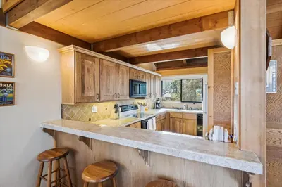 a kitchen with wooden cabinets and a counter with stools at Rocky Point # 4 - 2 BR Northstar Condo, Shuttle to Slopes, HOA Amenities! in Truckee