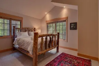 a bedroom with a wooden bed and two windows at Tahoe Time on North Shore - 4 BR Cabin w Private Hot Tub, Pet Friendly, Walk to Dining in Tahoe Vista