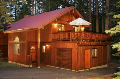 a large wooden cabin with a balcony and an umbrella at Tahoe Woods by Tahoe Getaways - Pet Friendly Tahoe Park Cabin w Hot Tub, Fireplace, Near Skiing! in Tahoe City