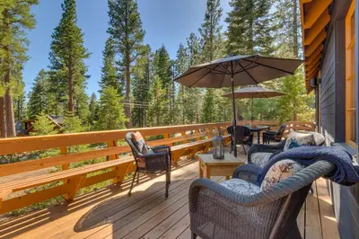 a deck with chairs and an umbrella on a house at Falcon's Rest - Ski and Summer Cabin in The Heart of North Lake Tahoe- Gas Fireplace in Carnelian Bay