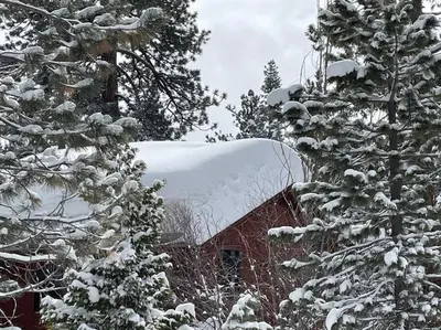 a snow covered roof of a red house with trees at Luna Cabin - 5BR Hot Tub A/C Game Room EV Charger in Tahoe Vista