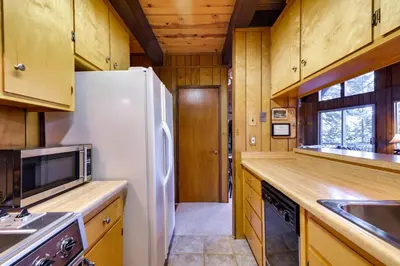a kitchen with a white refrigerator and wooden cabinets at 3 Mi to Big Trees State Park Cabin with Deck in Arnold
