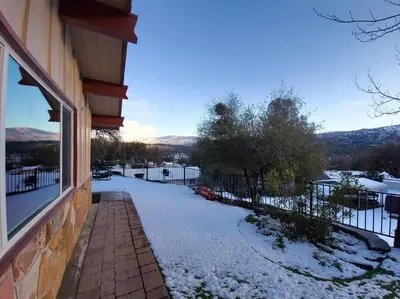 a house with a snow covered driveway next to a window at Yosemite Gateway Cottage - King Suite - Mountain Views in Oakhurst