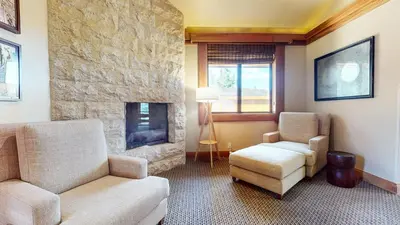 a living room with two chairs and a stone fireplace at Obsidian #1 home in Mammoth Lakes