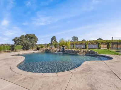 a pool with a waterfall in a yard at Luxury 4 Acre Estate - Pickleball, Pool, Hot Tub! in Lockeford