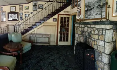 a living room with a stone fireplace and a staircase at Historic Dow Hotel in Lone Pine