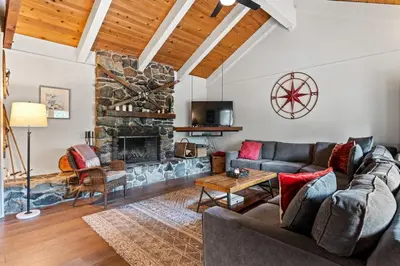 a living room with a couch and a stone fireplace at Trailblazer Chalet at Olympic Valley with Private Hot Tub and Ski Shuttle in Alpine Meadows