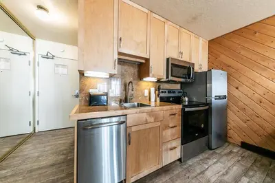 a kitchen with wooden cabinets and a stainless steel refrigerator at Lovely Studio w/Kitchen and Partial Lake View #122 at Donner Lake Village in Truckee