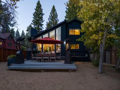 a black house with a table and an umbrella at Waves End Lakefront - 3BR Tahoe Vista w Private Sandy Beach, Walk to Town! in Tahoe Vista