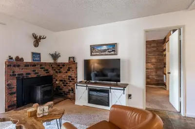 a living room with a tv and a brick fireplace at Cozy Cabin-Style Condo in Central Location in Mammoth Lakes