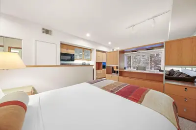 a bedroom with a large white bed and a kitchen at Palisades Tahoe Lodge Rentals Studio #234 in Olympic Valley