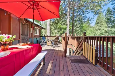 a wooden deck with a red table and an umbrella at Lewis Creek cabin near Yosemite king beds in Oakhurst