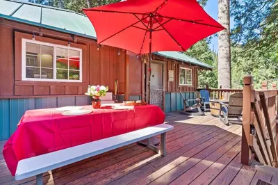 a table with a red umbrella on a deck at Sugar Pine cabin in the woods King bed Fire pit in Oakhurst