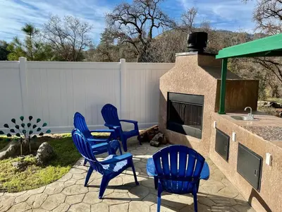a patio with four blue chairs and a fireplace at Peacock House Sleeps 12 Hot Tub Game Room in Ahwahnee