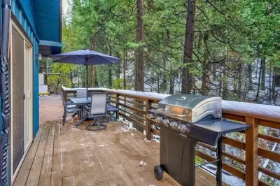 a grill on a deck with a table and an umbrella at Starlight Cabin in Oakhurst