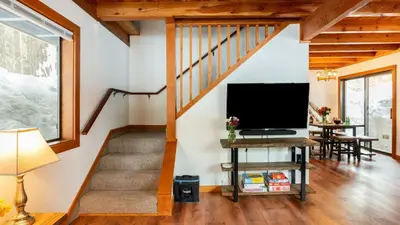 a living room with a staircase and a flat screen tv at Minutes to Skiing Lake Hot Tub Fire Pit Deck Indigo Owl by AvantStay in Homewood