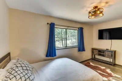 a bedroom with a bed and a window with blue curtains at 2 Mi to Mi-Wuk Village Cabin with Large Deck in Twain Harte